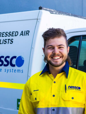 Compressor-Service-Technician-Perth-Jensen-2023 Nessco Pressure Systems (NPS) compressor service technician smiles and wears a high-vis yellow work shirt. He stands in front of a white NPS work vehicle.
