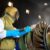 Abrasive blasting operator wearing protective equipment sandblasting a large metal industrial component using compressed air.